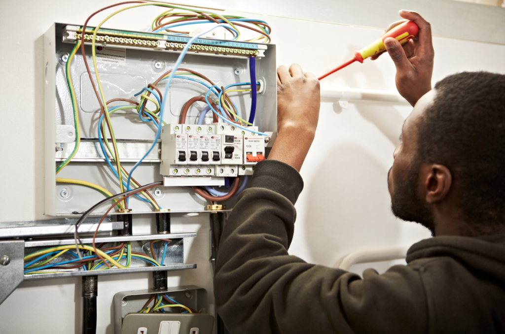 Able Skills student wiring from a fuse board during an electrical courses. They are holding a red and yellow electrical screwdriver and looking towards the area they are using the tool. 