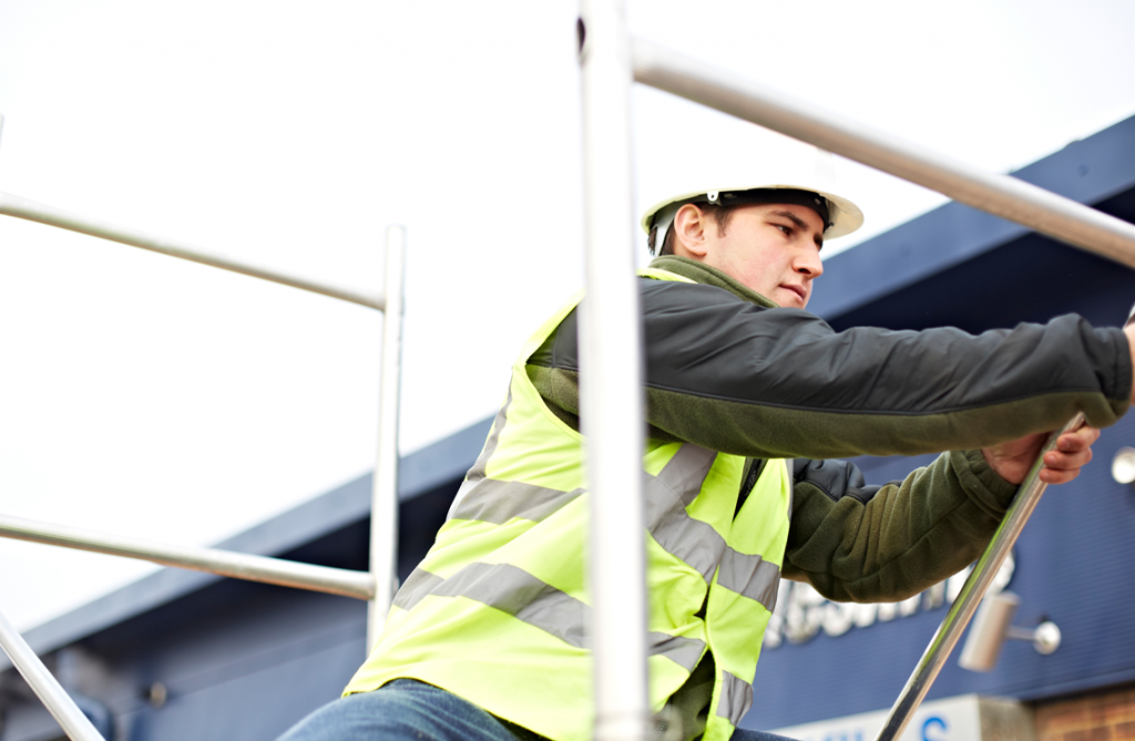 Construction worker wearing a hi-viz jacket and hard hat, working on a tower ladder