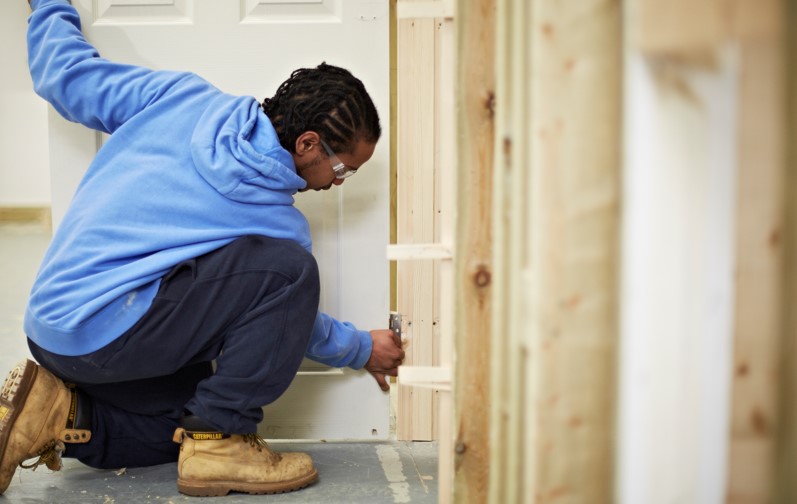 Person crouched down hanging a wooden door into a frame