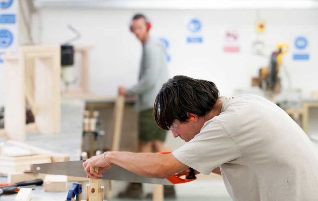 Person learning carpentry at Able Skills Construction Training Centre. They are using a saw to cut a piece of wood