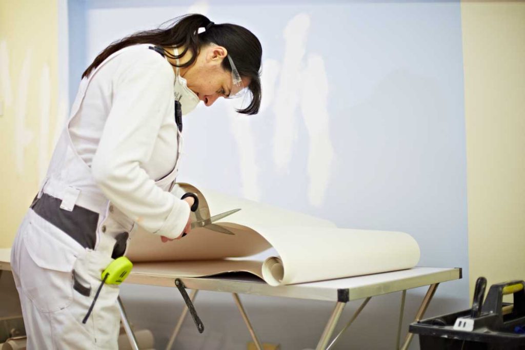 Person leaning over a table and cutting wallpaper