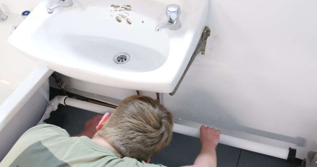 Plumber with their head under a white bathroom basin.