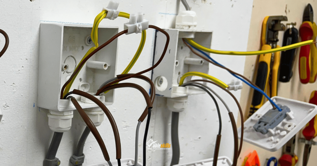 Electrical sockets on a wall, their fronts open and wires coming out of them. A selection of electrical tools hang on the wall next to them.