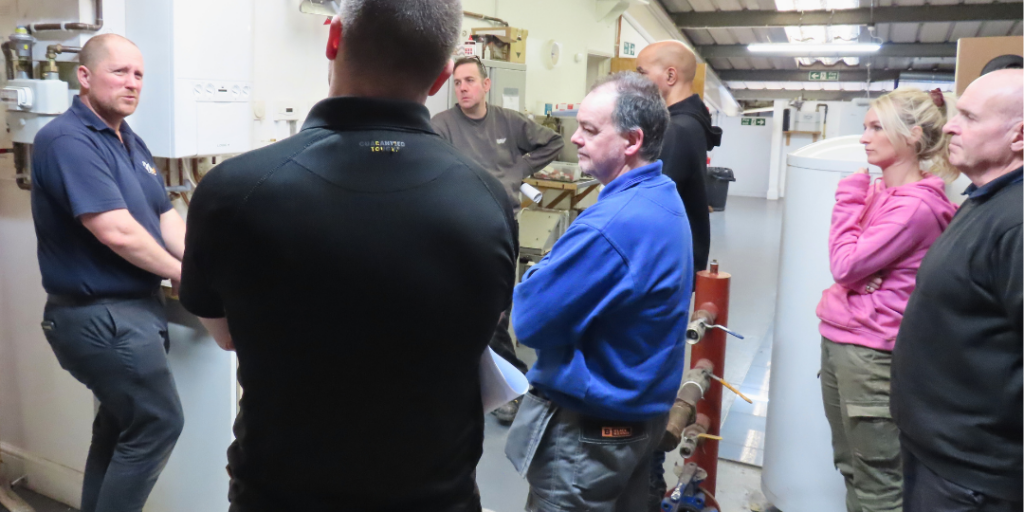 A group of plumbing students stand in a group and are listening to the instructor