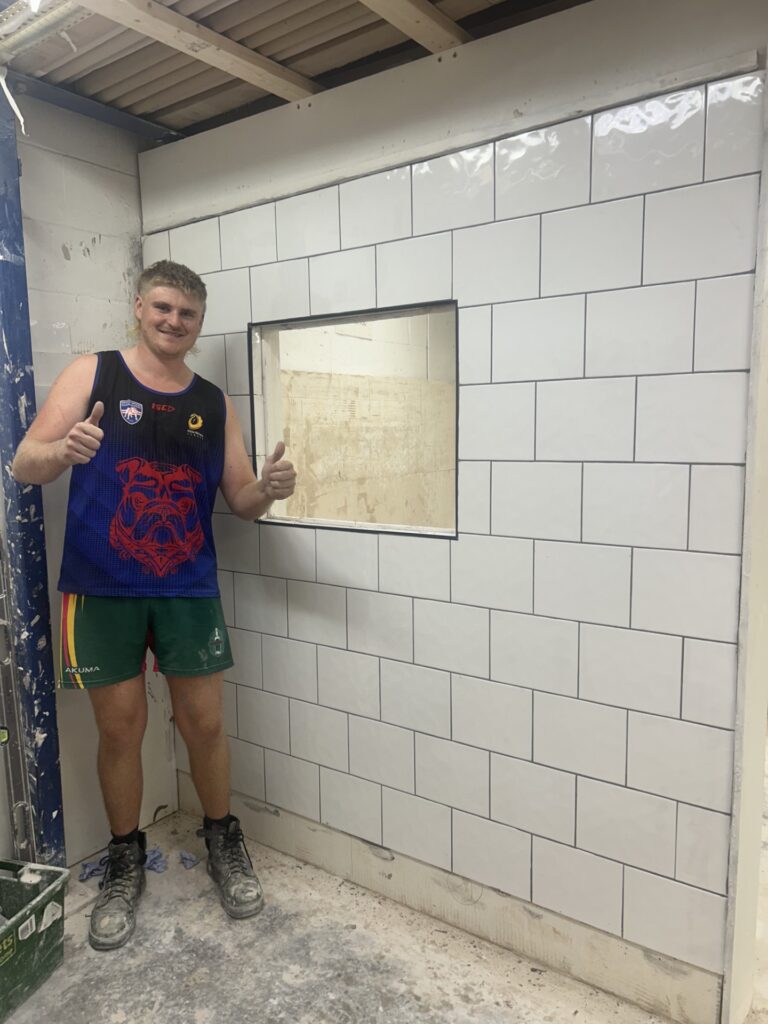 Jake standing in the tiling workshop at Able Skills in front of a newly tiled wall