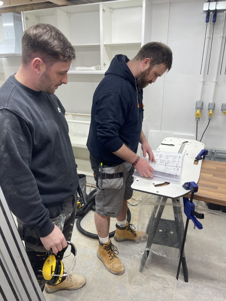 Two people are looking at a technical manual standing in a partially-installed kitchen at Able Skills