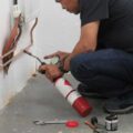 A person is doing plumbing, crouching down soldering copper pipes installing radiators in a bathroom